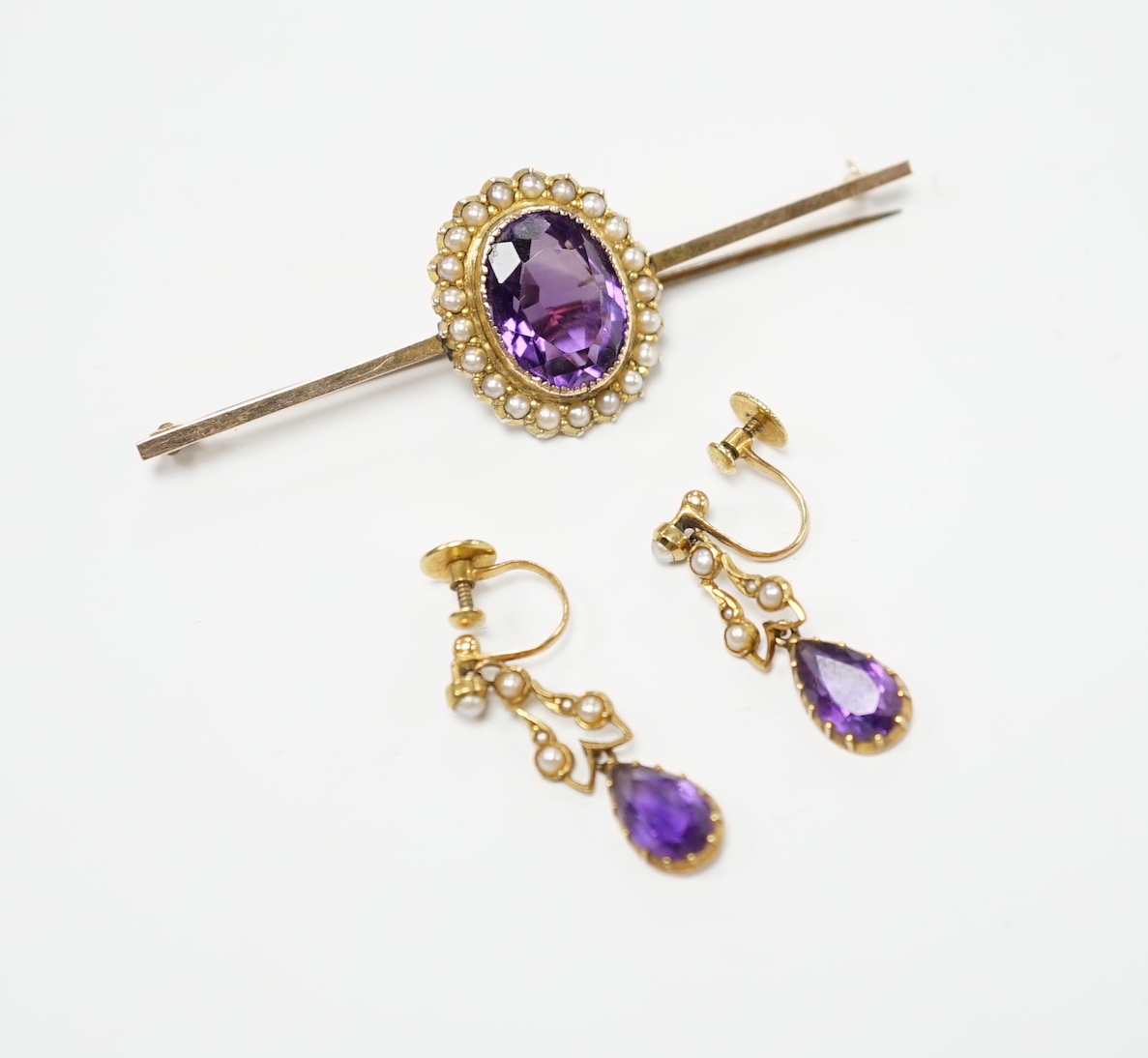 A yellow metal, amethyst and seed pearl cluster set bar brooch, 65mm and a pair of similar drop ear clips, gross weight 10 grams.